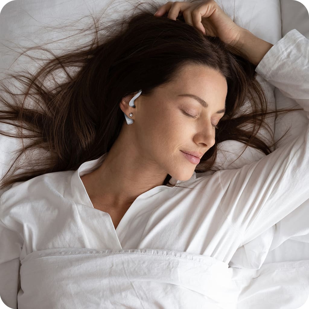 Pretty lady in bed wearing white and she is wearing SoundOff Noise Masking Earbuds