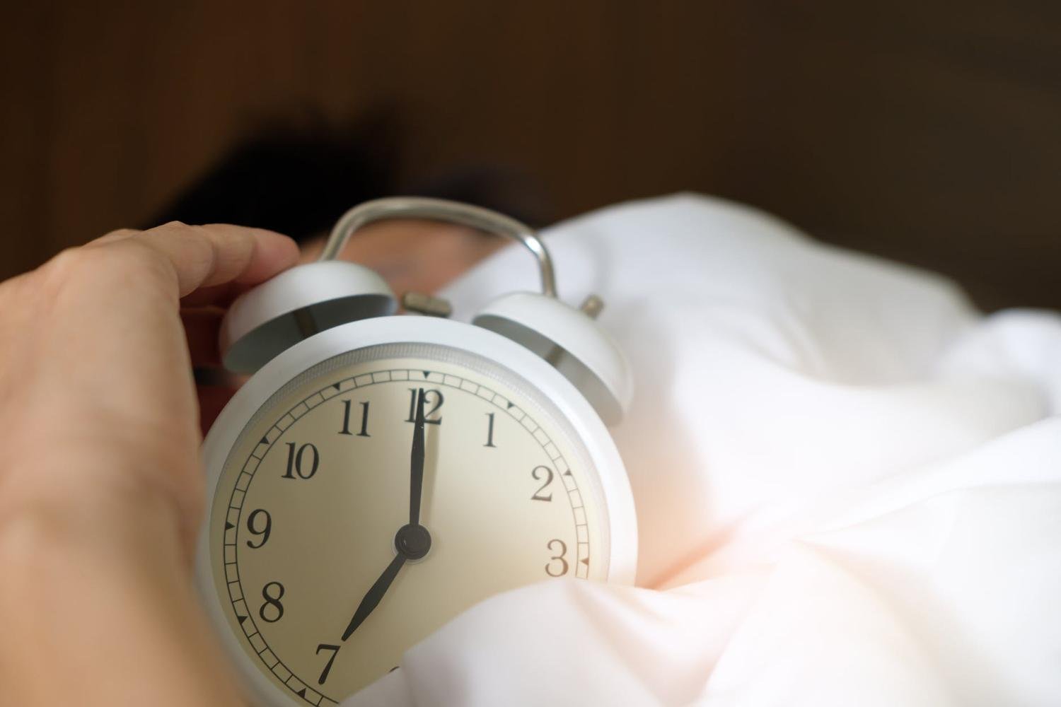 Alarm Clock held in mans hand showing 7:00AM